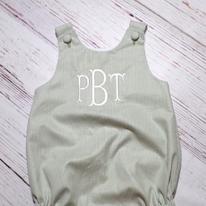 May include: A green and white gingham baby onesie with a white embroidered monogram "PBT" on the front.