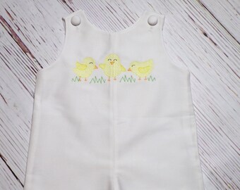 May include: White baby romper with three yellow embroidered chicks in a row, standing in green grass.
