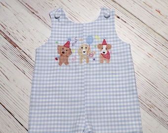 May include: Blue and white gingham baby romper with embroidered dogs wearing party hats. The dogs are holding a balloon and a lollipop.