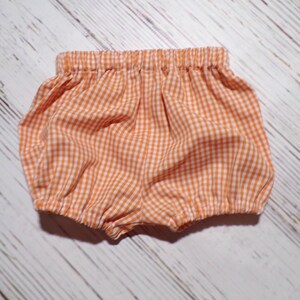 May include: Orange and white gingham baby bloomers with elastic waistband.