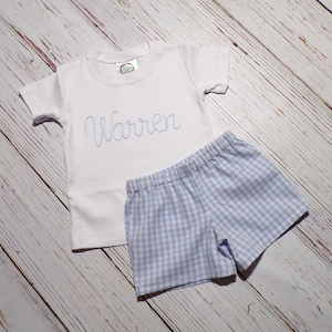 May include: A white short-sleeved t-shirt with the name "Warren" embroidered on the front, paired with blue and white gingham shorts.