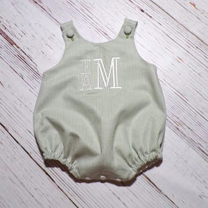 May include: A green and white gingham baby onesie with white embroidered letters "EM".