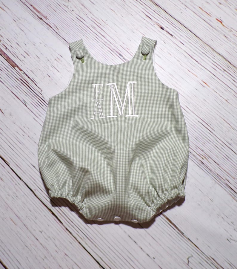May include: A green and white gingham baby onesie with white embroidered letters "EM".
