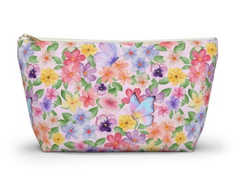 May include: A zippered cosmetic bag with a floral and butterfly pattern. The bag features a light pink background with colorful flowers and butterflies in shades of pink, purple, yellow, and blue. The zipper is gold-colored.