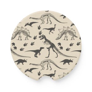 May include: A round beige car coaster with a black and white dinosaur skeleton pattern. The pattern includes various dinosaurs, including a T-Rex, a Stegosaurus, and a Triceratops, along with dinosaur footprints.