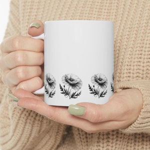 Puede incluir: Taza de cerámica blanca con un diseño de flores de amapola en blanco y negro alrededor del borde.
