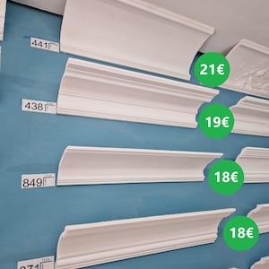 Puede incluir: Molduras de yeso blanco de varios tamaños y estilos con etiquetas de precios en euros. Las molduras se muestran en una pared azul. El texto "PietroStucchi FABBRICA MANUFATTI IN GESSO" y un icono de WhatsApp con el número "3483880946" están en la parte inferior de la imagen.