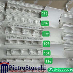 May include: A display of white plaster mouldings with intricate designs, including curved and straight pieces. Prices are listed in euros next to each moulding.