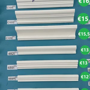 May include: White decorative crown molding samples, varying in design and size, are displayed against a teal background. The image includes the company logo and contact information. The molding pieces range from 2 to 5 inches wide.