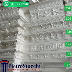 Può includere: Un'esposizione di modanature in gesso bianco con disegni intricati, tra cui cherubini e motivi floreali. Le modanature sono etichettate con prezzi in euro. Il testo "PietroStucchi FABBRICA MANUFATTI IN GESSO" è visibile nella parte inferiore dell'immagine.