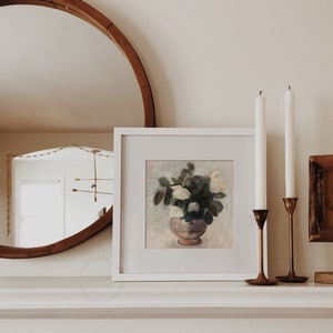 Neutral Flower Still Life Painting on a Fireplace Mantel, with a round mirror and varying heights of candles in a warm living room decor. | Dear Alice Digital Art