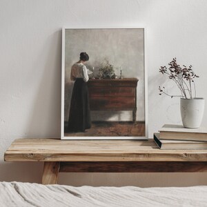 Printable Art of a European Portrait Painting featuring a woman seen from behind reading a book. The white modern frame is laid on an antique wooden bench in a muted farmhouse bedroom. | Dear Alice Digital Art