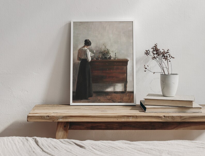 Printable Art of a European Portrait Painting featuring a woman seen from behind reading a book. The white modern frame is laid on an antique wooden bench in a muted farmhouse bedroom. | Dear Alice Digital Art