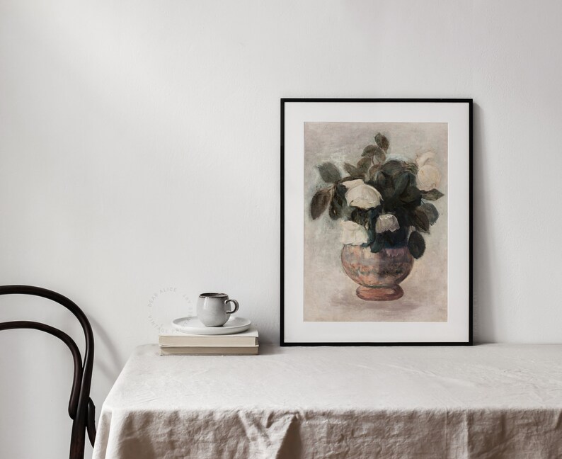 Neutral colors Painting of a bouquet of white roses, framed and displayed on a table covered with a linen tablecloth, a chair and a cup of coffee on top of a pile of book. | Dear Alice Vintage Art