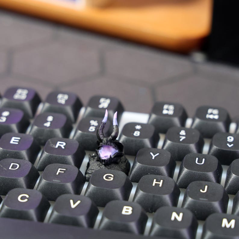 Puede incluir: Una peque&ntilde;a figura miniatura negra y morada con cuernos en un teclado negro.