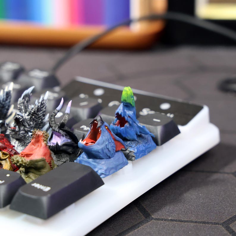 Puede incluir: Un teclado con varias teclas de monstruo de colores. Las teclas est&aacute;n impresas en 3D y presentan diferentes dise&ntilde;os de monstruos, incluyendo un monstruo verde con una cabeza puntiaguda, un monstruo azul con la boca muy abierta y un monstruo rojo con un hocico largo y puntiagudo.
