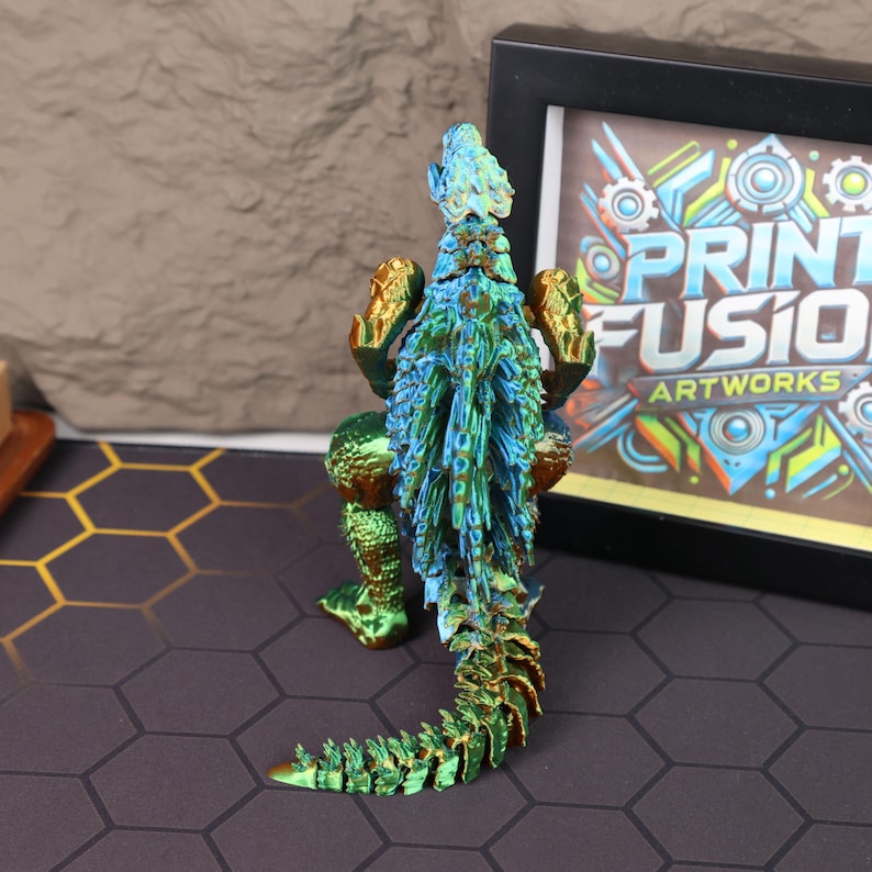 Angled top-down shot of the blue-green electroplated Godzilla figure displayed on a wooden shelf, surrounded by other collectible items. The photo captures the overall proportions of the figure, its vibrant metallic finish, and the attention to detail in the dorsal plates and body texture. This Godzilla figure is an excellent addition to any monster-themed room, gaming station, or collector display setup, designed to appeal to fans of Japanese kaiju, sci-fi films, and 3D printed art.
