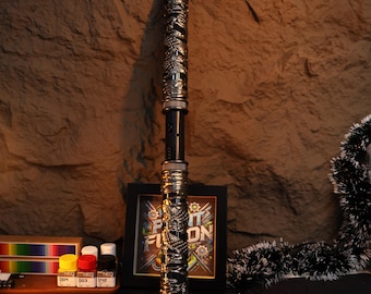 May include: A black and gold metal staff with intricate dragon designs. The staff is about 30 inches long and has a black handle.