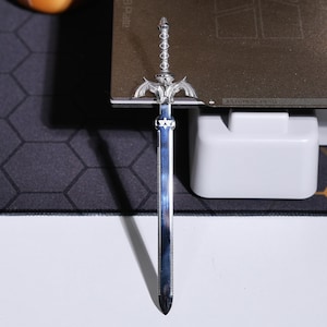 May include: A silver-colored sword with a detailed hilt and a sharp point. The sword is on a gray surface.