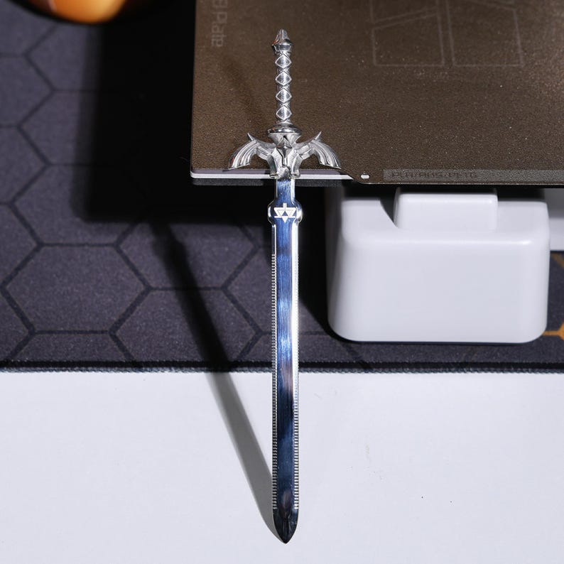 May include: A silver-colored sword with a detailed hilt and a sharp point. The sword is on a gray surface.