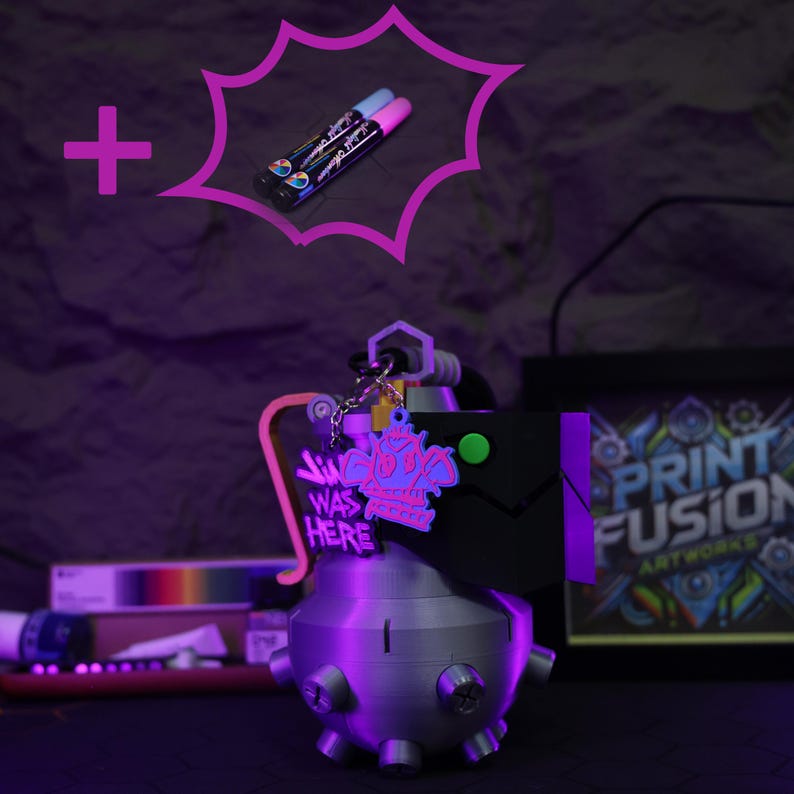 May include: A 3D printed gray grenade keychain with a black and green tag that says "Jim Was Here" and a pink and purple cartoon character. The keychain is on a dark purple surface with two pink and purple markers in the background.