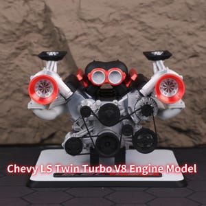 May include: A detailed model of a Chevy LS Twin Turbo V8 engine. The engine features silver, black, and red components, including twin turbos with red accents and a complex belt system. The model is mounted on a white base with the text "Chevy LS Twin Turbo V8 Engine Model".
