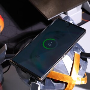 May include: A black smartphone with a fingerprint sensor is charging on a wireless charging pad. The phone's screen shows a green charging circle with the text "42%".