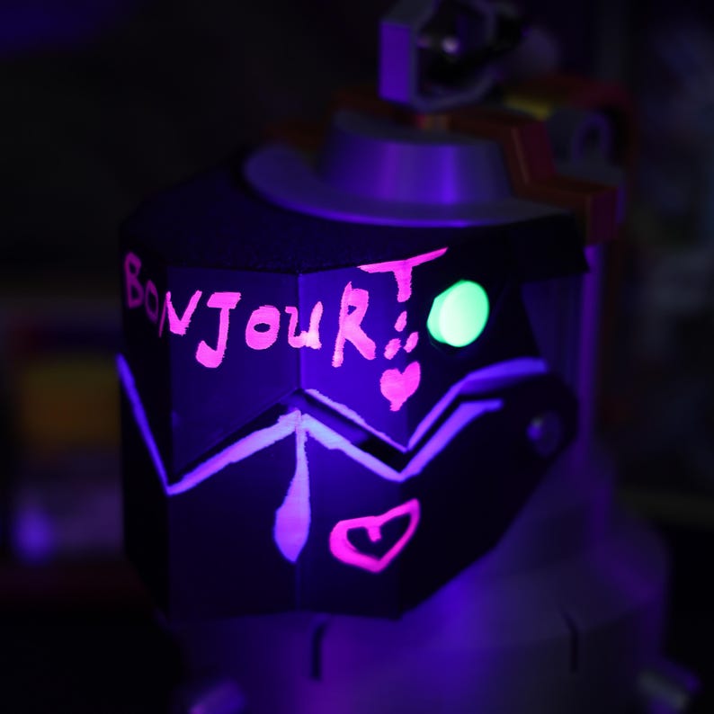 May include: A black, geometrically shaped object with a pink inscription that reads "Bonjour!" and a green glow. The object has two pink hearts drawn on it.