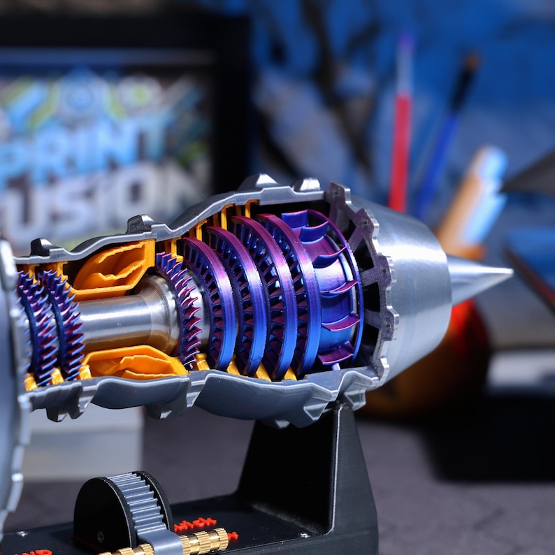 Op de afbeelding: Een gedetailleerd doorsnedemodel van een straalmotor met een zilver, blauw en oranje kleurenschema. Het model is gemonteerd op een zwarte standaard en toont de interne werking van de motor.