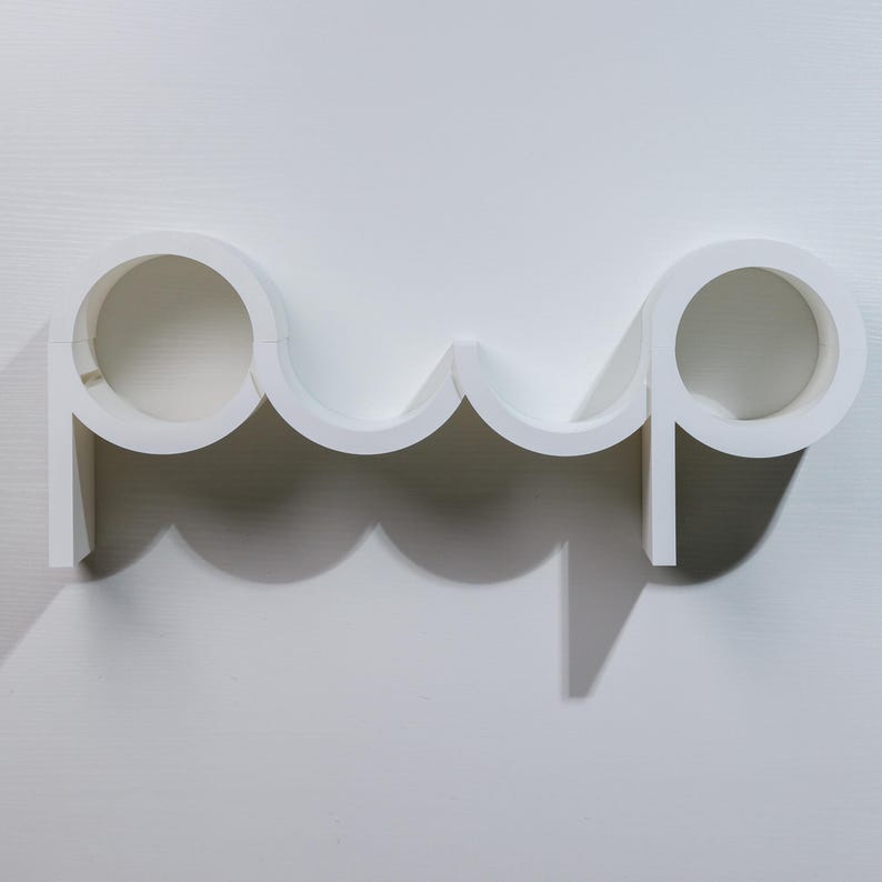 May include: White wall-mounted shelf unit shaped like the word "pop" with three circular openings.