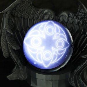 Side angle shot of the custom LED crystal ball on a gothic angel wings base, illuminating a desk setup filled with gaming gear and anime merchandise. The image emphasizes the orb's mystical glow and modern USB-C charging port, making it a functional yet decorative piece for fantasy lovers, gamers, and anyone wanting a holiday gift idea that’s personal and stylish.