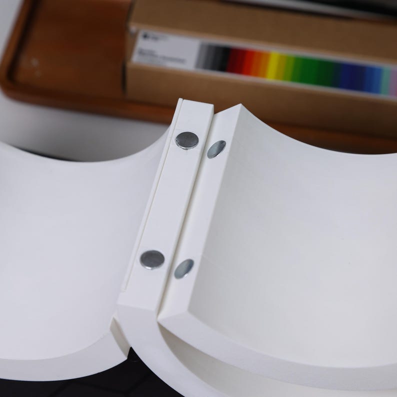 May include: Two white curved shelves with magnetic closures. The shelves are attached to each other and are made of a smooth, white material.