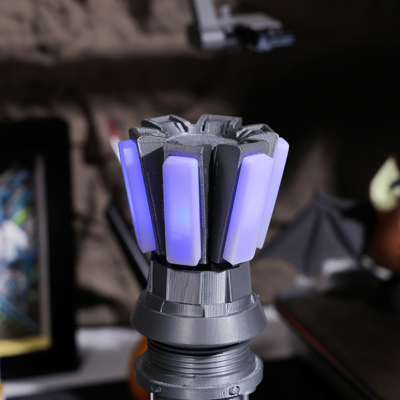 Puede incluir: Una empu&ntilde;adura de sable de luz impresa en 3D de color gris con una funci&oacute;n de iluminaci&oacute;n azul. La empu&ntilde;adura tiene un dise&ntilde;o en forma de estrella con m&uacute;ltiples paneles que emiten un brillo azul.
