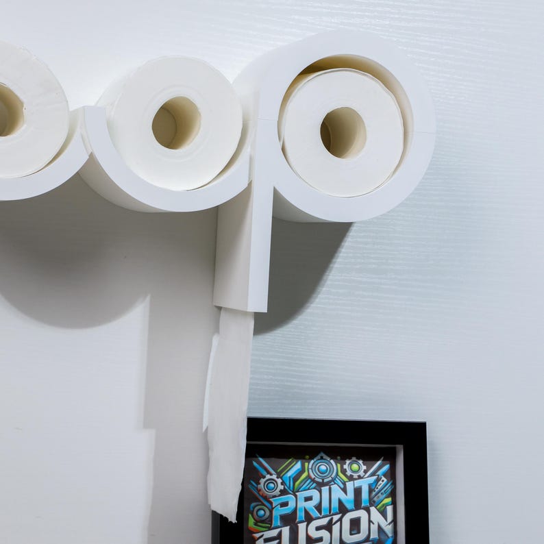 May include: White wall-mounted toilet paper holder with three rolls of toilet paper. One roll is partially unrolled and hanging down. The holder is shaped like the word "loop".