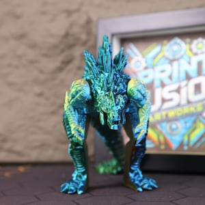 Electroplated Godzilla kaiju figure posed on a display shelf with soft lighting highlighting its shimmering blue-green chrome finish, showcasing the detailed dorsal spines, textured body, and articulated limbs. The 3D printed collectible is shown standing tall and fierce, making it an ideal centerpiece for any sci-fi or monster-themed collection. This fully poseable figure is designed for Godzilla fans, platform gamers