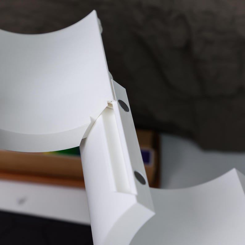 May include: White plastic shelf unit with two curved shelves. The shelves are connected by a white plastic piece with two black dots on the side.