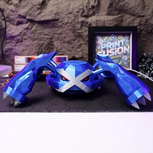 May include: A blue and white 3D printed model of a Pokemon character. The character has a large, flat head with a white X across the eyes. The character has four arms and is standing on a black surface.
