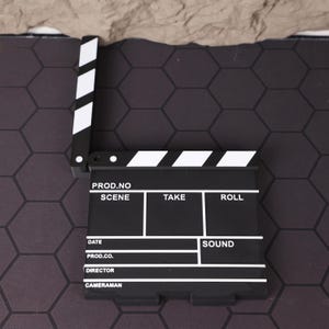 Angle shot of the miniature folding director’s chair, highlighting the printed logo on the fabric and the clean structure of the 3D print. This item is a great gift for aspiring directors, producers, and anyone studying or working in film. It serves as a daily reminder of your creative vision and love for cinema. Perfect for holiday gifting, birthdays, or special occasions for those passionate about storytelling and film production aesthetics.