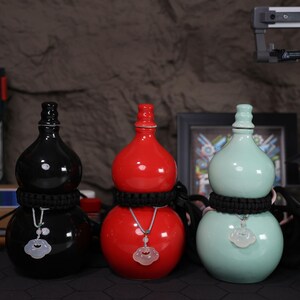 May include: Three ceramic gourd-shaped bottles with black, red, and green glaze. Each bottle has a black cord tied around the middle and a jade pendant hanging from the cord.