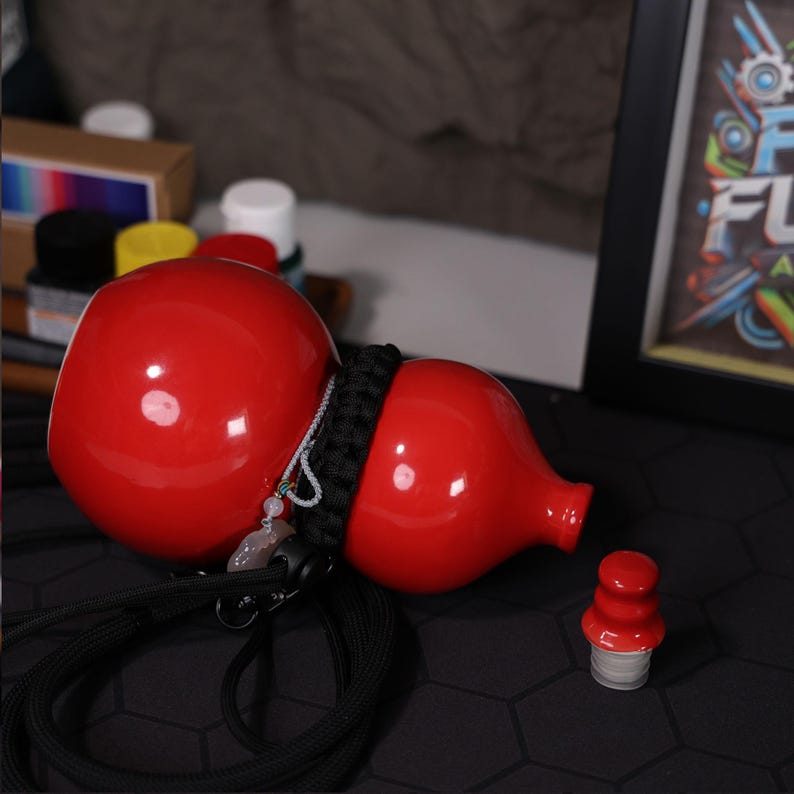 May include: A red gourd-shaped bottle with a black cord and a red bottle cap. The bottle has a shiny, glossy finish.