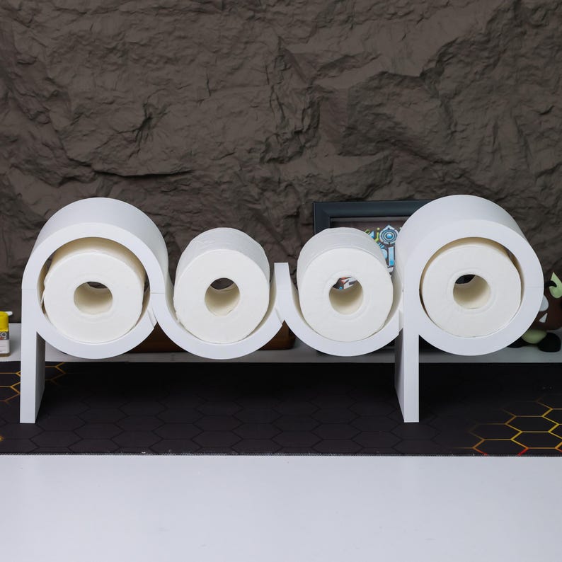 May include: White toilet paper holder shaped like the word "poop" with three rolls of toilet paper on it.