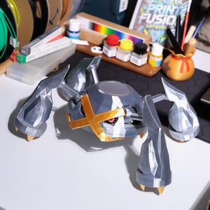May include: A 3D printed model of a grey and silver robotic creature with a gold cross on its head. The creature has four legs and a round body.