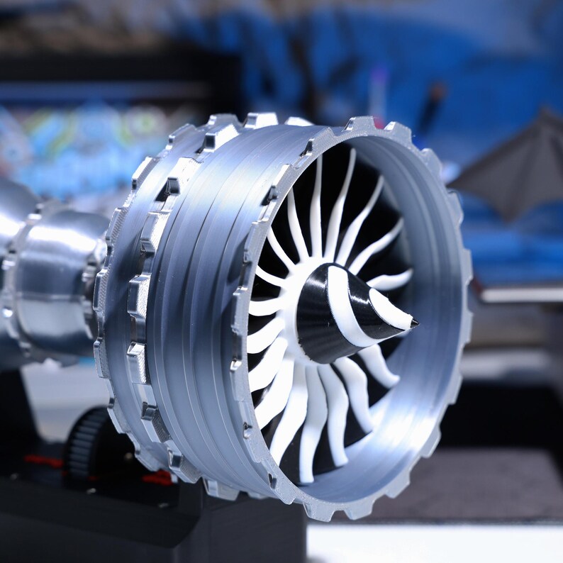 Op de afbeelding: Een close-up van een model straalmotor met een zilveren behuizing en een witte ventilator. De ventilator is gemaakt van plastic en heeft een zwart midden.