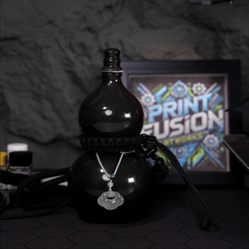 May include: A black ceramic gourd-shaped bottle with a silver chain and pendant. The bottle is decorated with a black paracord strap and a black cord.