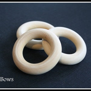 May include: Three unfinished wooden rings, stacked on top of each other, on a black surface. DIY Bows.