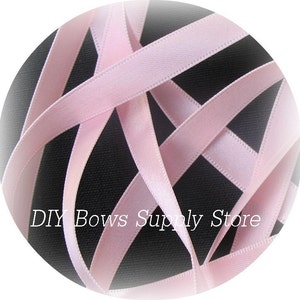 Könnte beinhalten: Rosa Satinband, 6 mm breit, in einem Kreis auf schwarzem Hintergrund. DIY Bows Supply Store ist auf dem Hintergrund gedruckt.