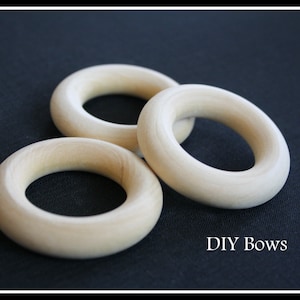 May include: Three pale wooden rings on a dark background. The rings are smooth and circular with a central hole. The text "DIY Bows" is visible in the image.