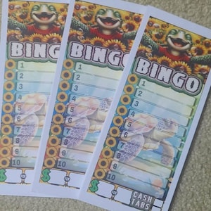 May include: Three bingo cards with a cartoon frog wearing a red shirt and surrounded by sunflowers. The word "BINGO" is at the top, with numbers 1-10 below. The bottom has the words "CASH TABS".