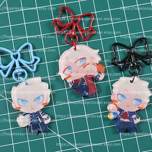 Op de afbeelding: Vijf anime-stijl acryl sleutelhangers met een personage met wit haar en blauwe ogen. De sleutelhangers hebben een cartoonontwerp en zijn bevestigd aan rode, zwarte en blauwe strikvormige sluitingen. De achtergrond is een groen raster.