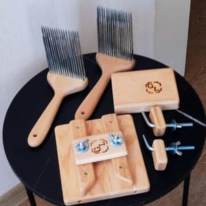 May include: A collection of wooden fiber tools for crafting. The set includes two large wool combs with metal tines, two wooden blocks with metal hardware, and a small wooden block with a logo. The tools are arranged on a black table.